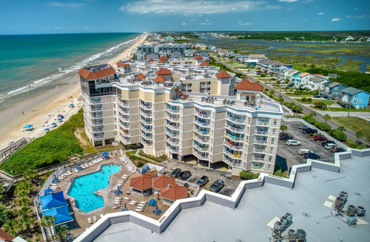 A wide exterior view shows the beachfront, a large swimming pool, residential buildings, and the ocean in the distance. Families are seen gathering by the pool and strolling along the beach, creating an inviting, communal vacation atmosphere.