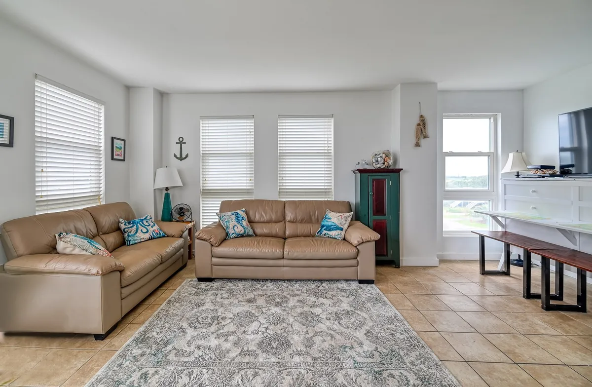 A casual and comfortable living room setting with two leather sofas, a textured area rug, decorative pillows, and large window views. The arrangement invites relaxation, family gatherings, and adaptable use for additional sleeping space if needed.