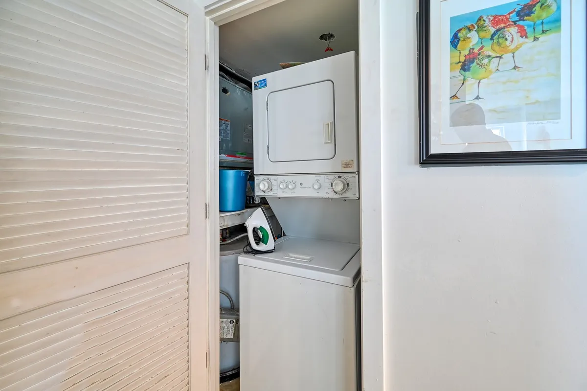 A tidy laundry closet featuring a stacked washing machine and dryer, accented by colorful wall art. The space is compact and efficient, with shelves for laundry supplies and a bright, practical atmosphere.