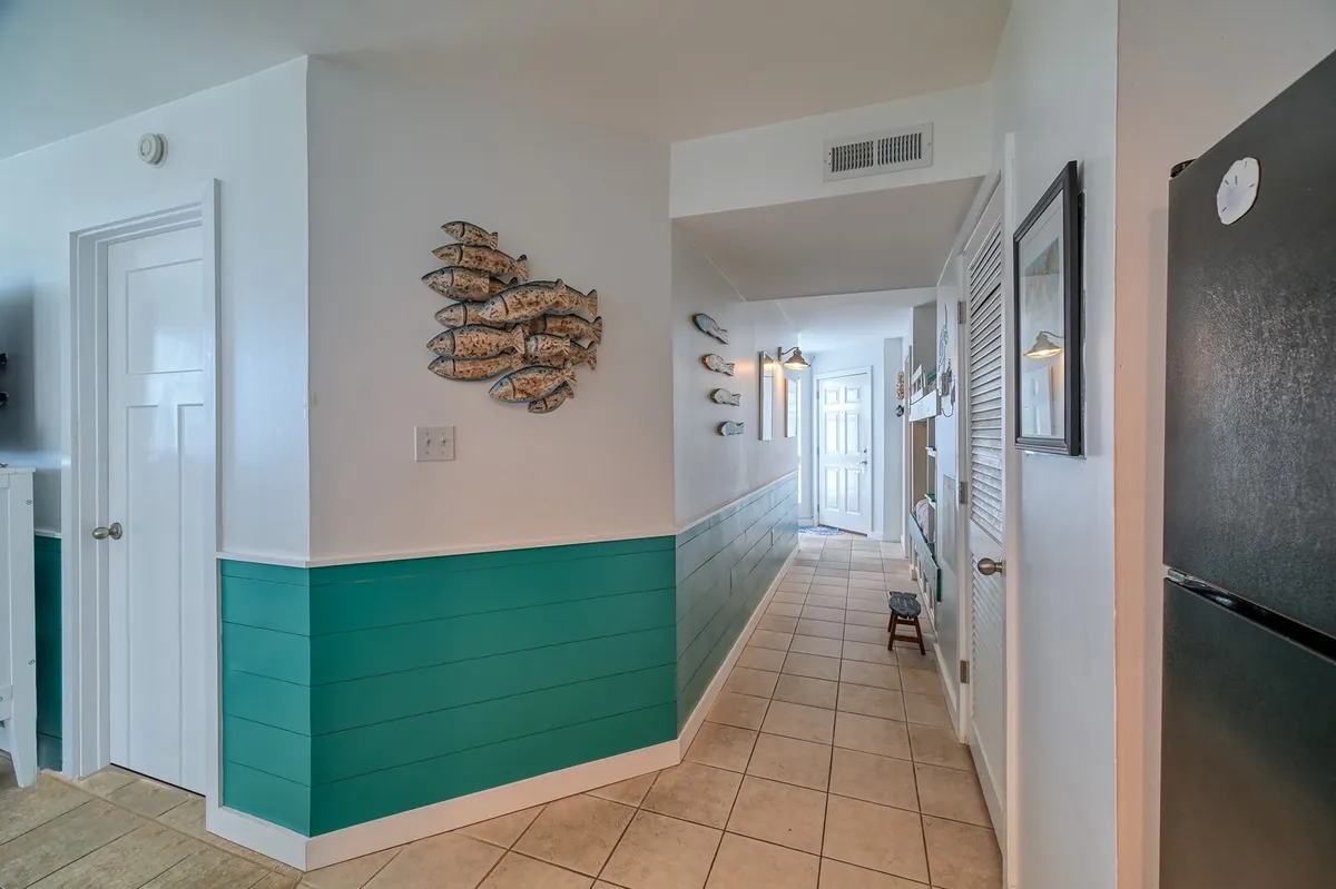 A cheerful, inviting interior hallway with teal wainscoting, decorative fish wall art, and plenty of natural light. The bright space is designed for socializing, with a relaxed and welcoming vibe.